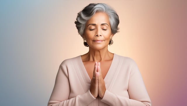 A woman with short, gray hair and closed eyes holds her hands in a prayer position against her chest. She wears a light pink, V-neck sweater and exudes calmness.